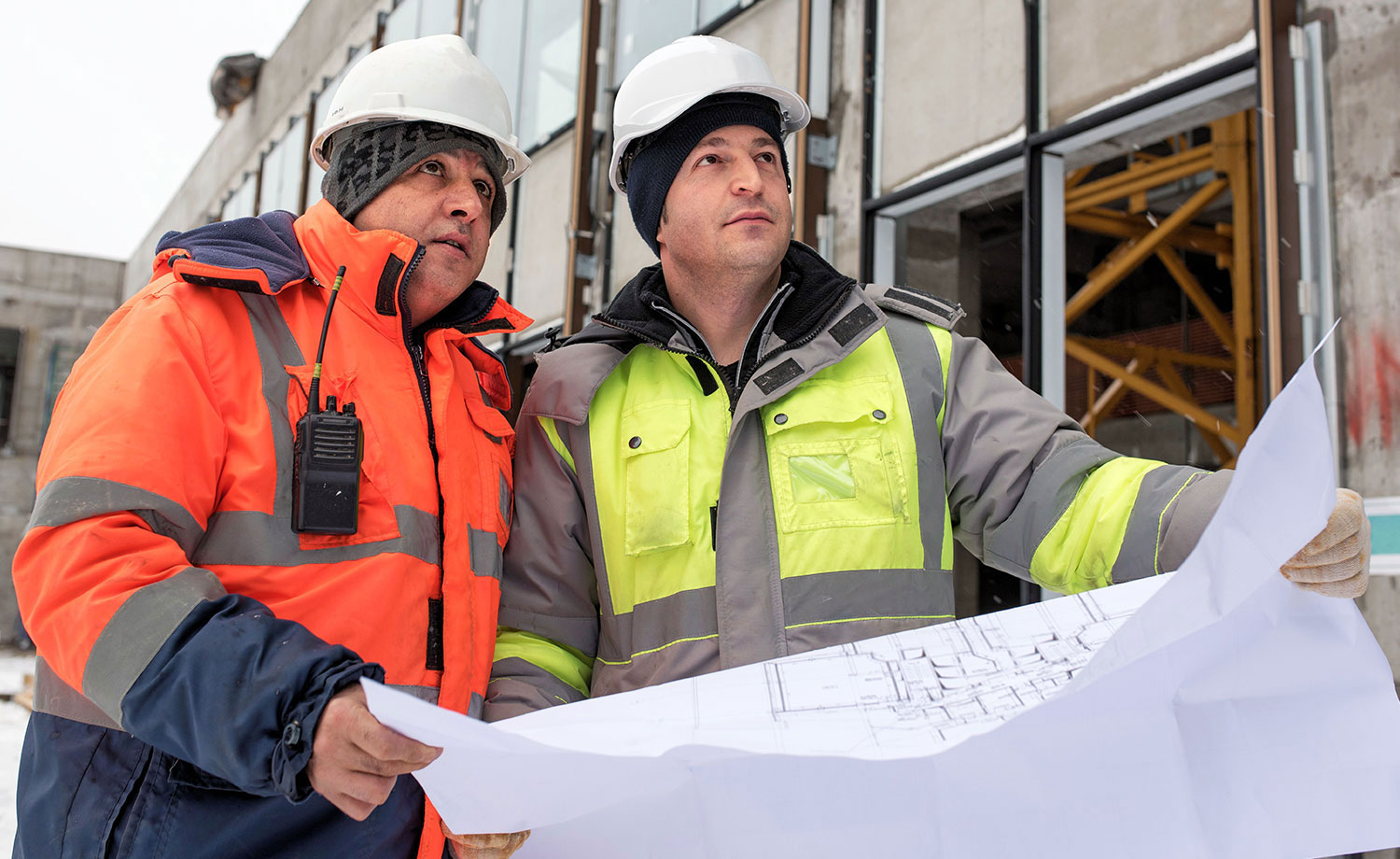 Two men in hard hats looking over plans.