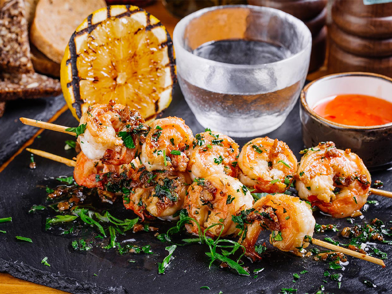 shrimp kebab skewers next to a grilled lemon and glass of water