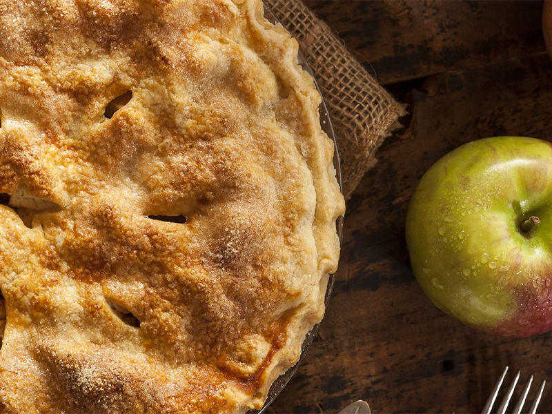 Apple pie next to an apple on a table top