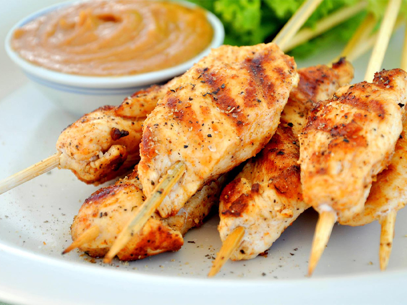 Grilled chicken skewers on a plate next to peanut butter dipping sauce