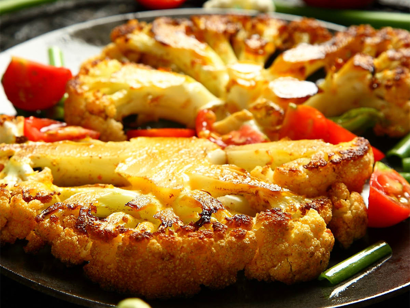 grilled cauliflower steaks on a plate with red pepper slices