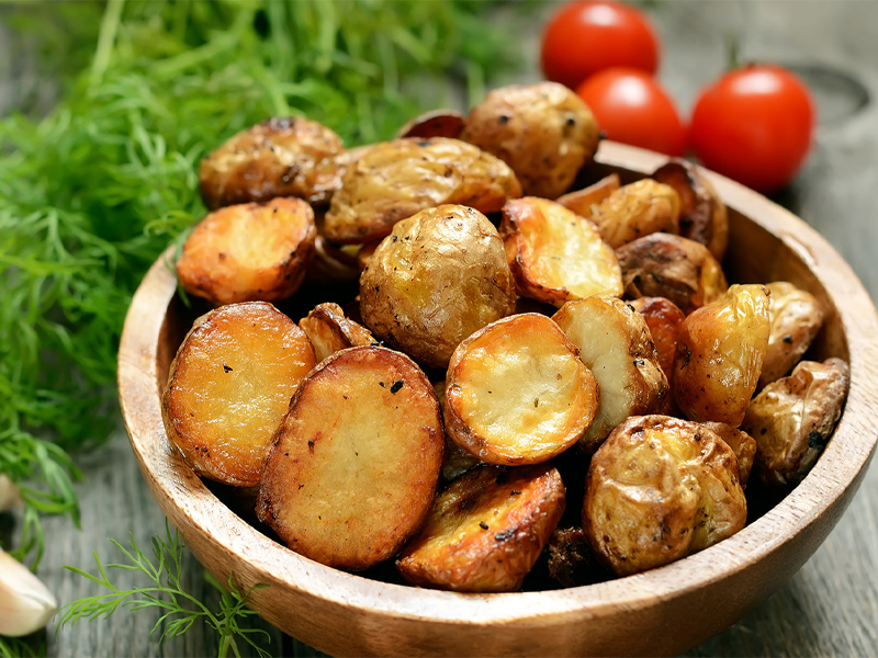 grilled new potatoes in a bowl near cherry tomatoes and greens