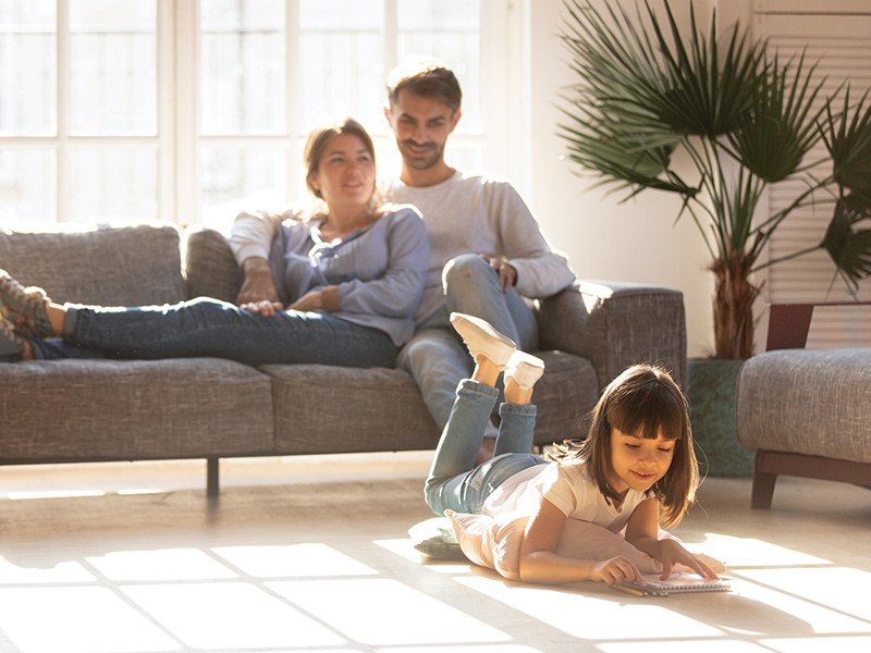 Child reading on the floor while parents look on from the sofa in propane heated home