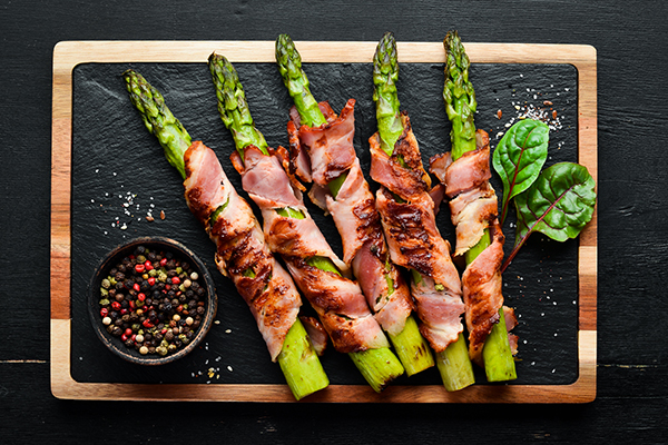 Bacon Wrapped Asparagus on Wood cutting board with spicy marinade