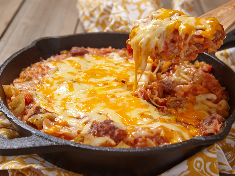 Cheesy Beef Mixture in Cast Iron Skillet being scooped with a wooden spoon