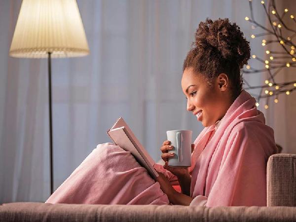 Woman cozy while drinking tea and reading in her robe with her thermostat set for winter