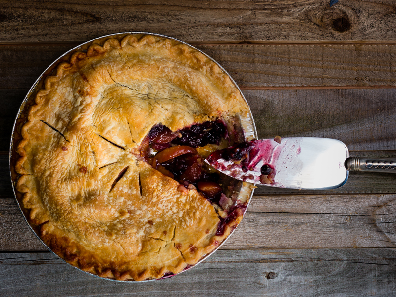 a whole blueberry pie with a slice taken out of it