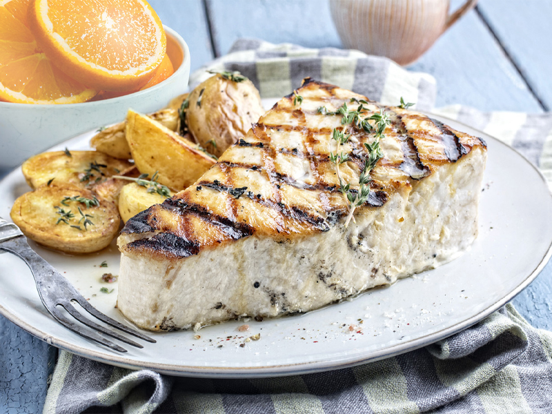 Grilled Swordfish on a white plate with oranges and parsley for garnish