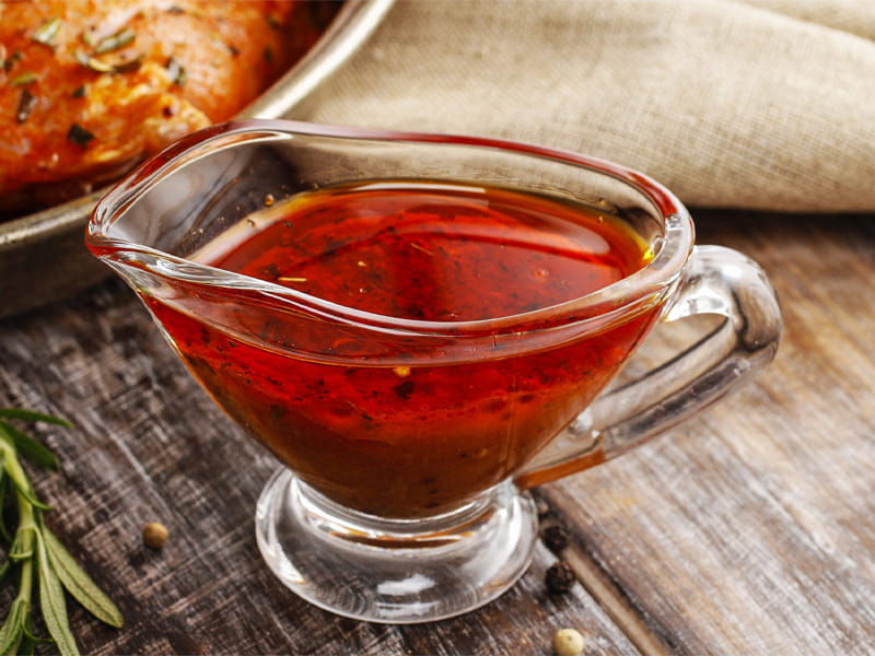 Honey Sriracha marinade in a glass bowl on a table with herbs and a linen napkin in the background