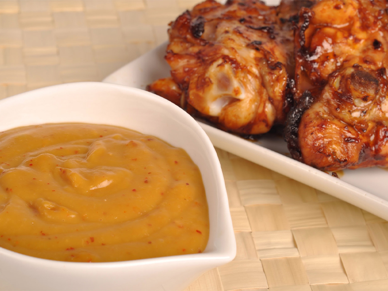 Grilled chicken on a plate next to a bowl of apricot glaze