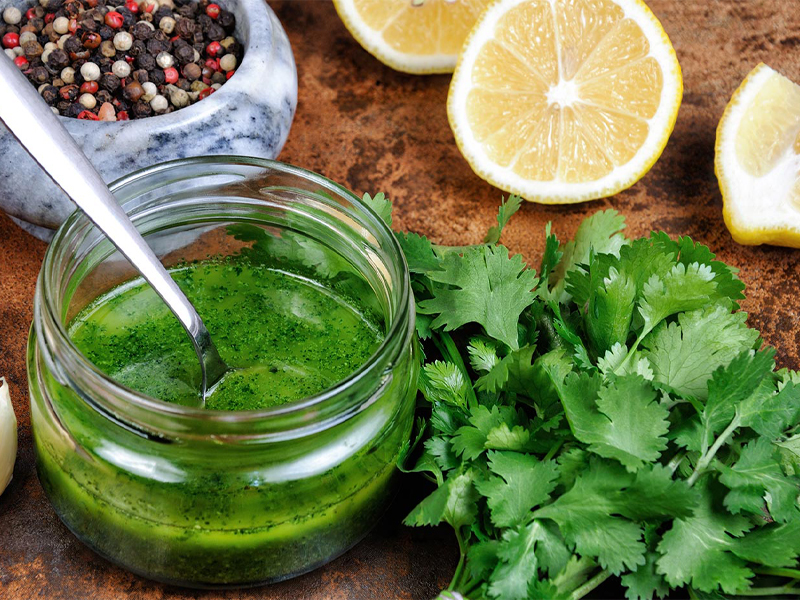 Green mojito marinate in a jar with a spoon on a cutting board with fresh parsley lemon and peppercorns