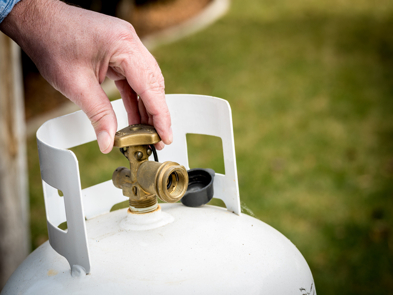 A person's hand tightening the knob on a propane grill tank