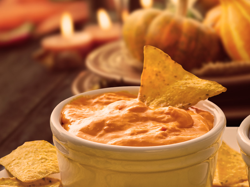 Pumpkin cheese dip in ramekin with tortilla chips with fall squash and tealights in the background
