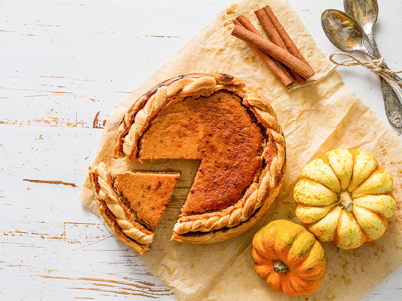 pumpkin pie with a slice cut out next to mini pumpkins and cinnamon sticks