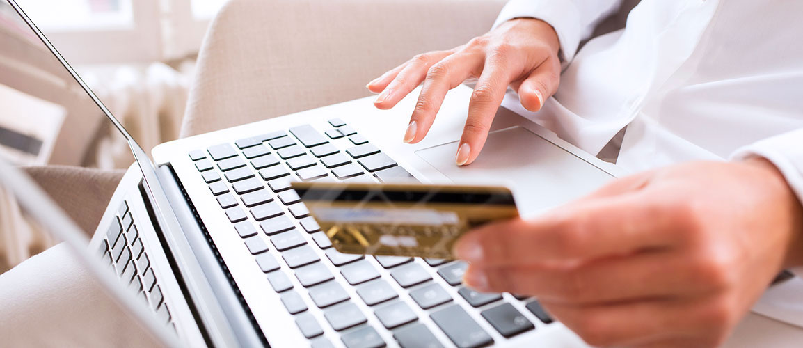 Person holding credit card in front of a laptop.