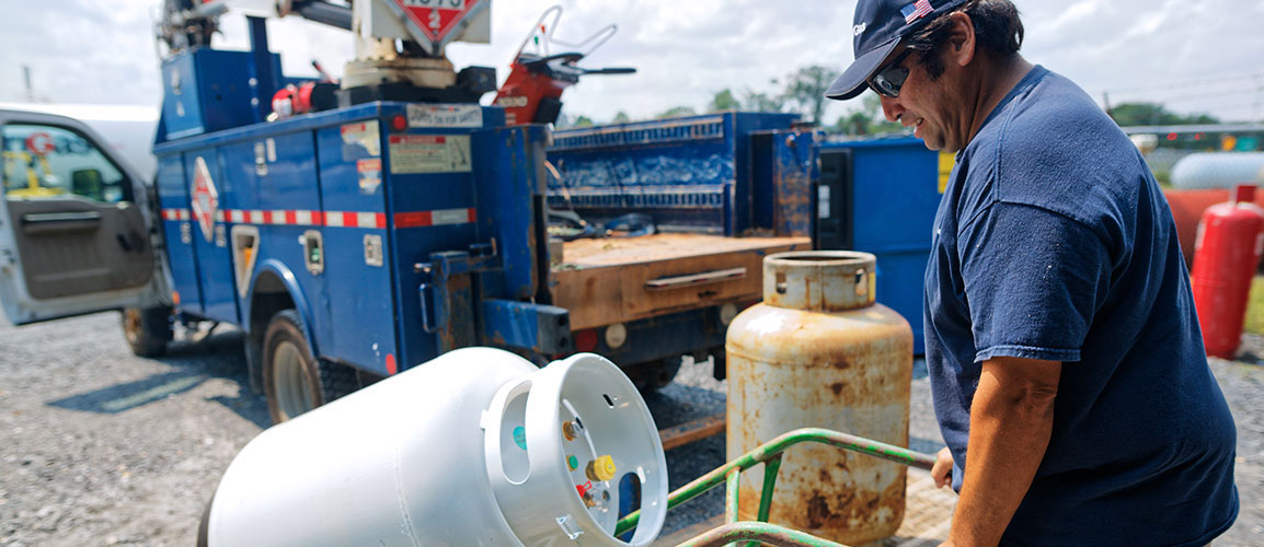 Man moving propane tank with a hand truck.