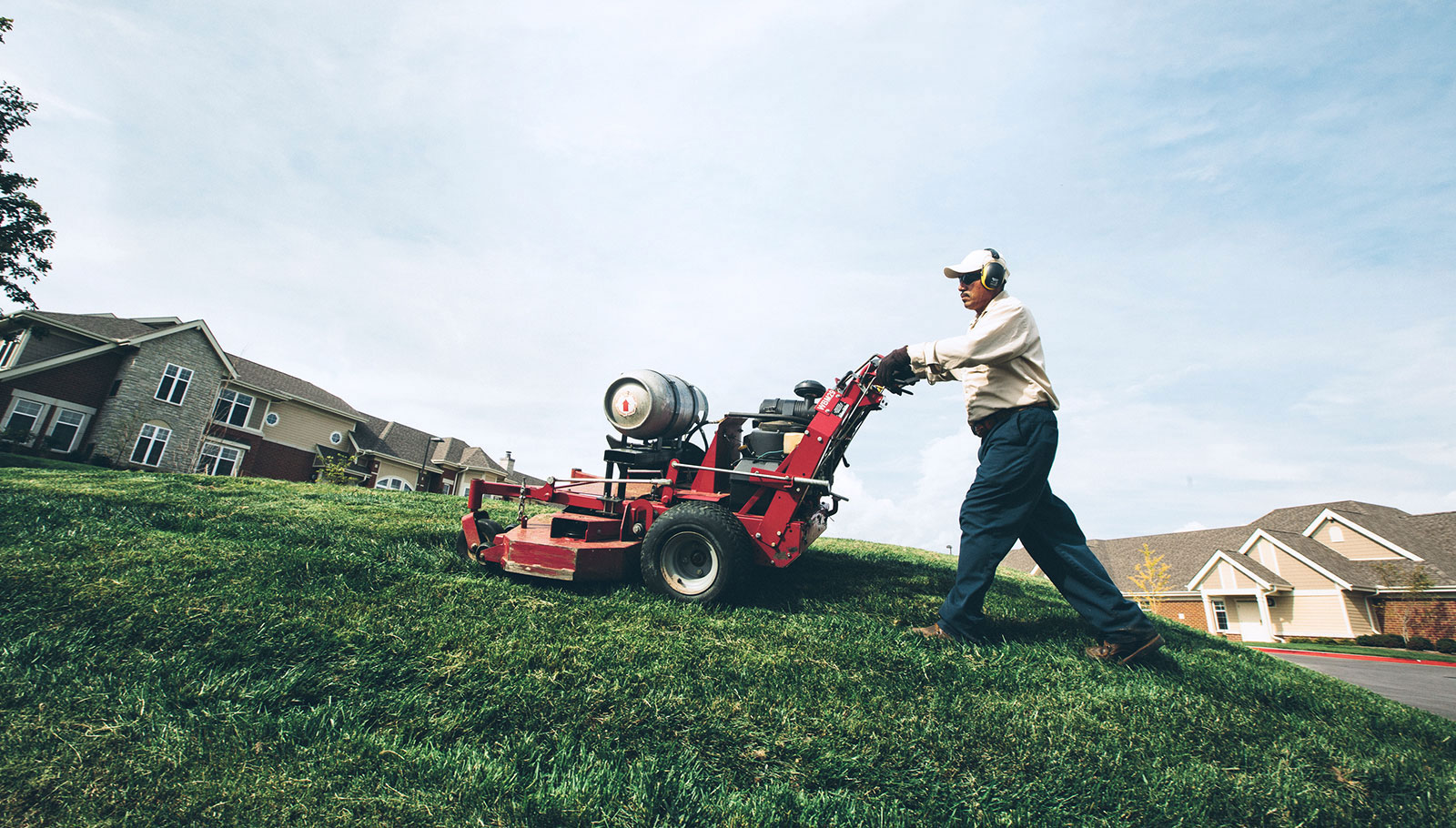 Man pushing propane powered lawn mower uphill.