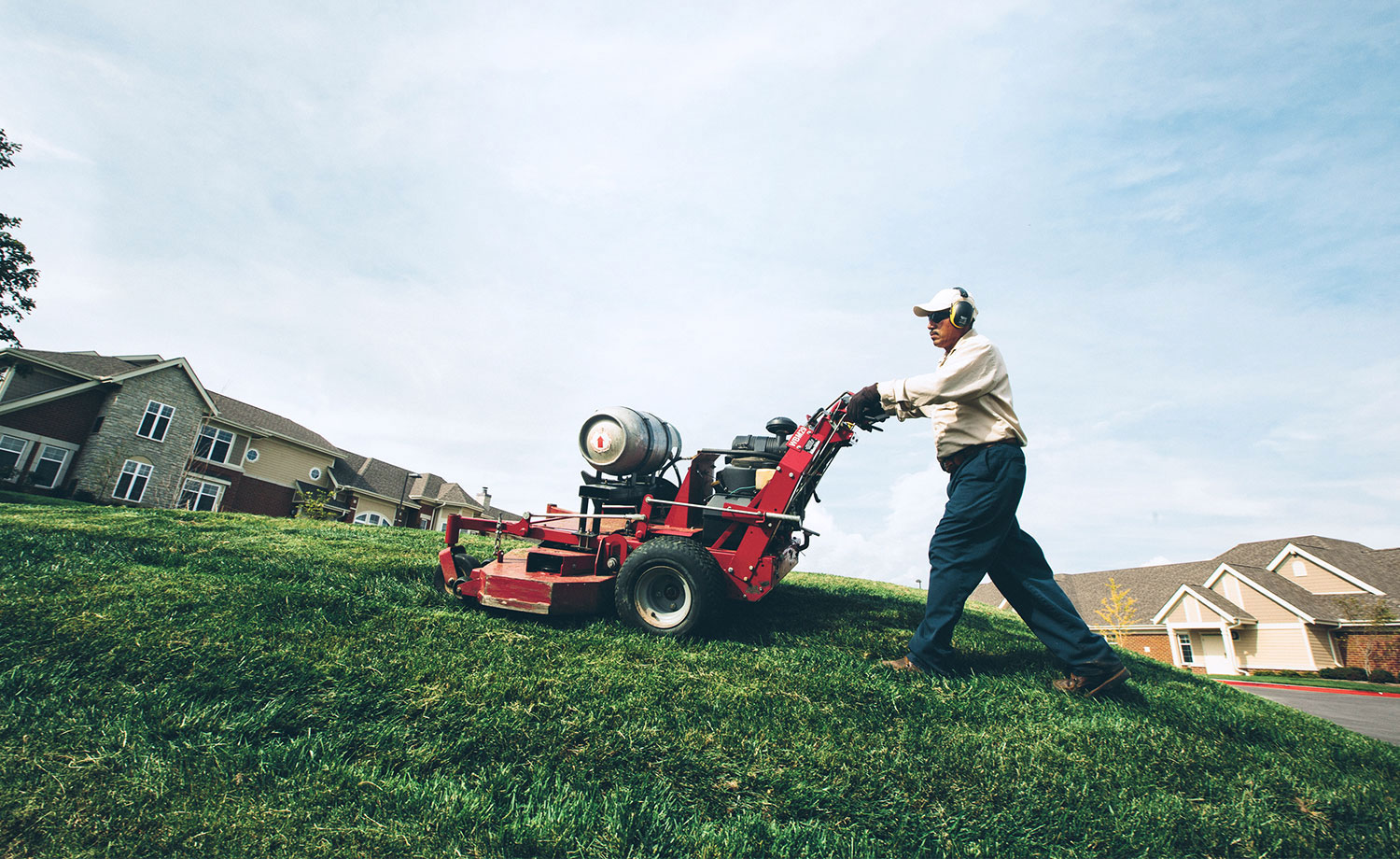 Man pushing propane powered lawn mower uphill.