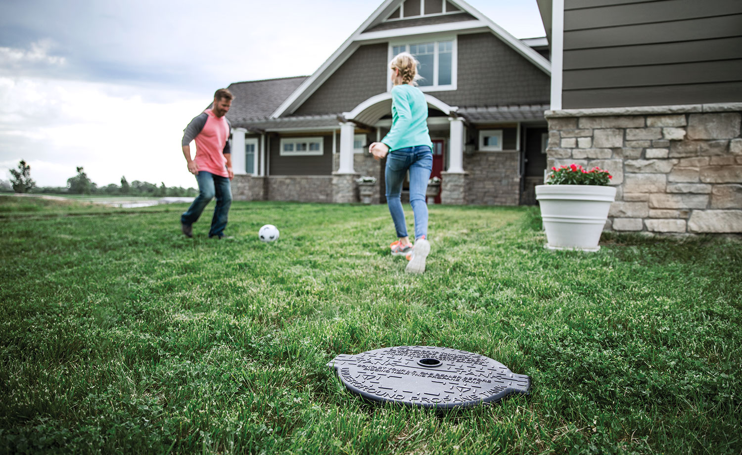 Man and daughter playing in a backyard near an underground propane tank lid
