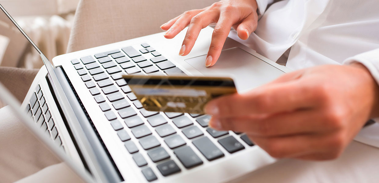 Person holding credit card in front of a laptop.