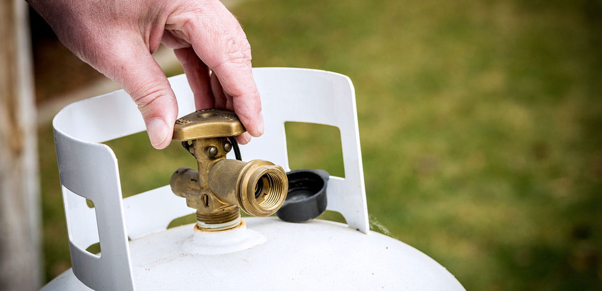 A hand turning the propane tank valve.